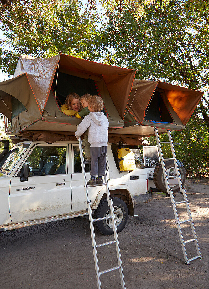 Boys standing on a ladder to a roof tent on a off-road vehicle, Nata, Nxai Pan National Park, Botswana