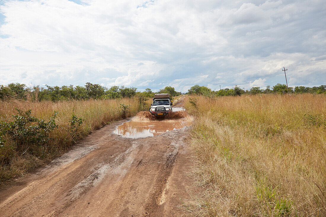 Geländewagen fährt auf Piste durch Wasserpfütze, Kazuma-Pan-Nationalpark, Livingstone, Simbabwe