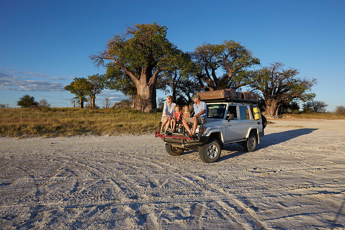 Family sitting on a off-road vehicle at sunset, Tutume, Nxai Pan National Park, Botswana