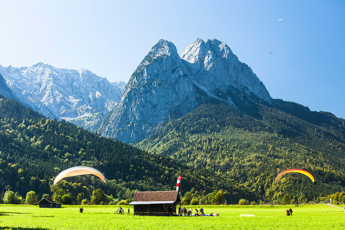 Paragliders landing on a meadow overlooking Waxenstein, Garmisch-Partenkirchen, Bavaria, Germany