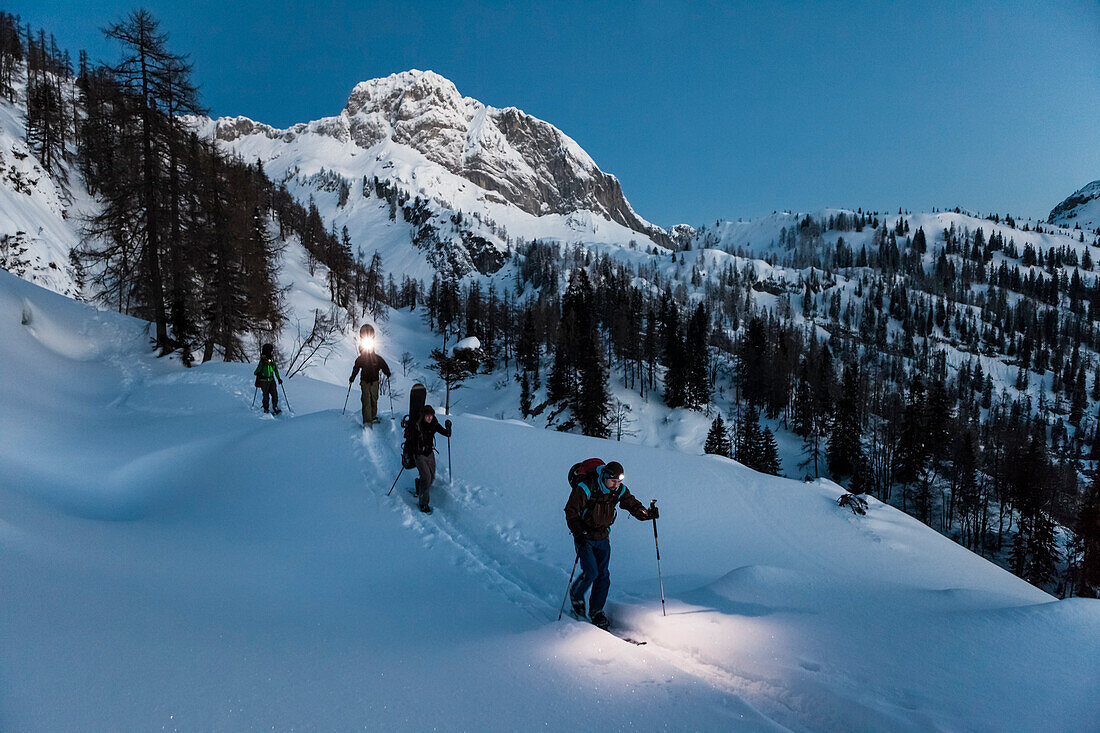 Skitourengeher mit Stirnlampen bei Morgendämmerung im Tennengebirge, Salzburg, Österreich