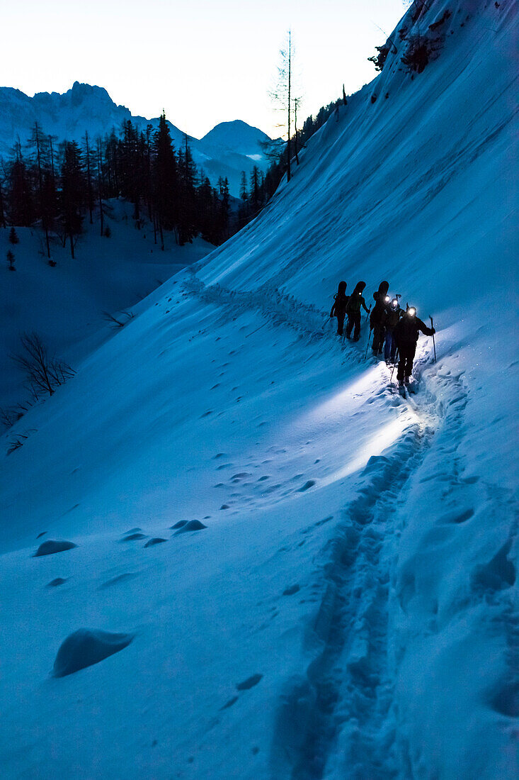 Skitourengeher mit Stirnlampen bei Morgendämmerung im Tennengebirge, Salzburg, Österreich