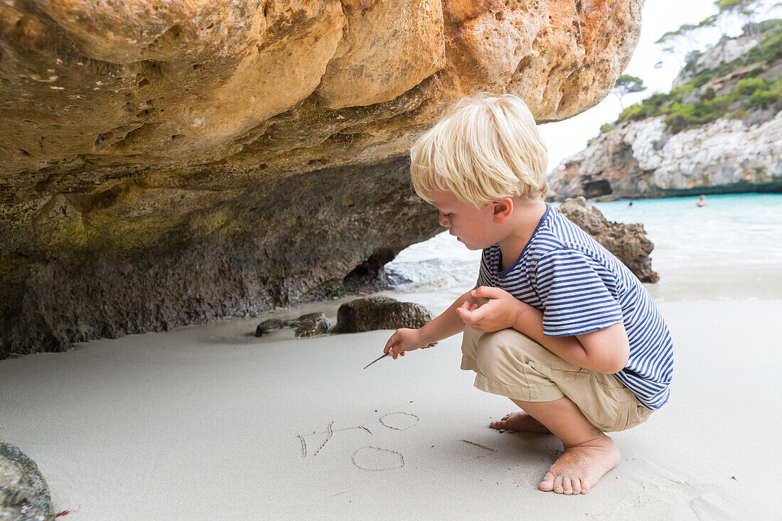 Junge schreibt in den Sand, Strand bei Calo des Moro, Mittelmeer, MR, bei Santanyi, Mallorca, Balearen, Spanien, Europa