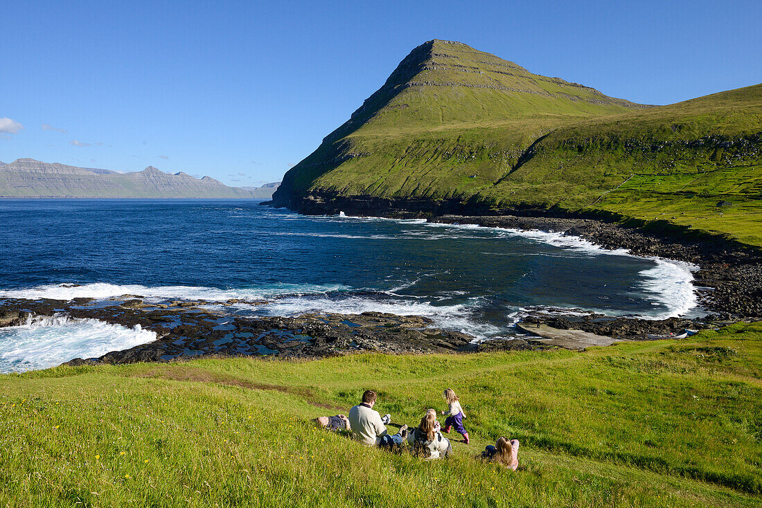 Family sitting in the grass overlooking the bay of Gjogv, Eysturoy Island, Faroe Islands