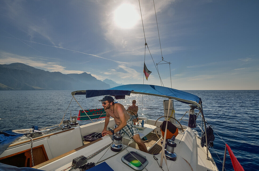 Two young men steering a sailing yacht, one is at the steering wheel, the other one trimming the sails by operating the winch, Mallorca, Balearic Islands, Spain, Europe