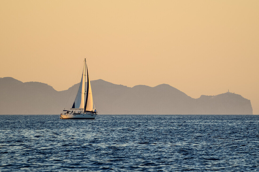 A sailing yacht at sunset, Cap Formentor with its lighthouse in the background, the northernmost point of  Mallorca, Balearic Islands, Spain, Europe