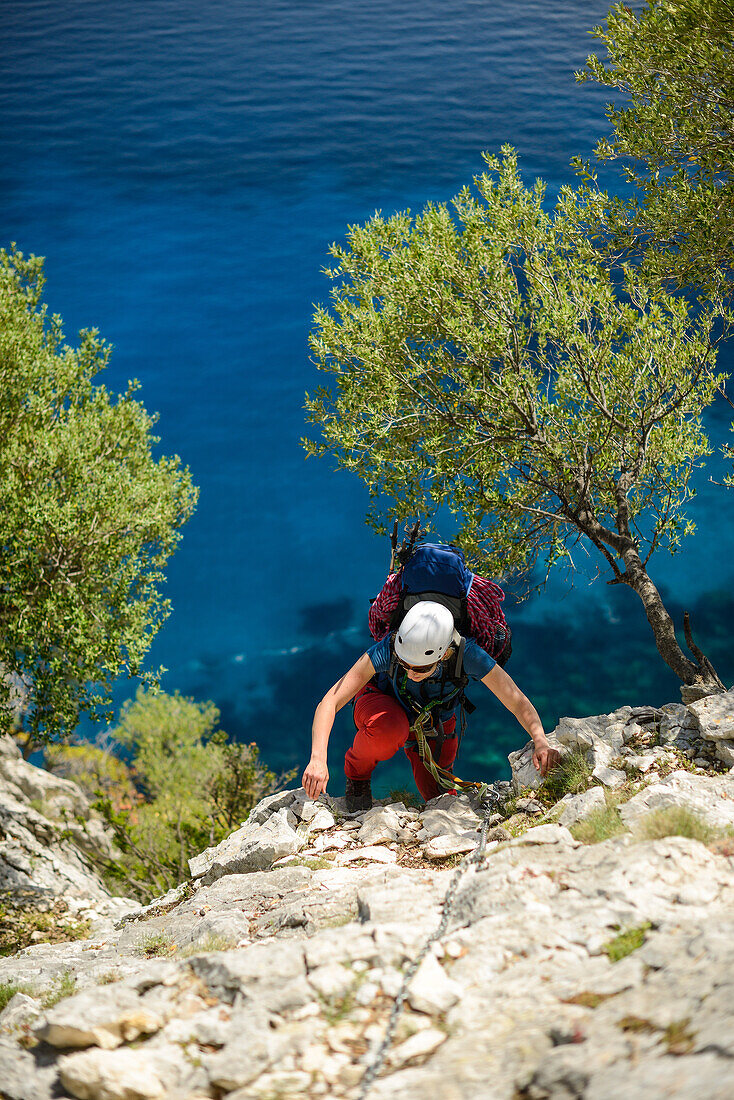Frau klettert eine steile Wand über dem Meer mit Kette versichert hinauf, Selvaggio Blu, Golfo di Orosei, Sardinien, Italien, Europa