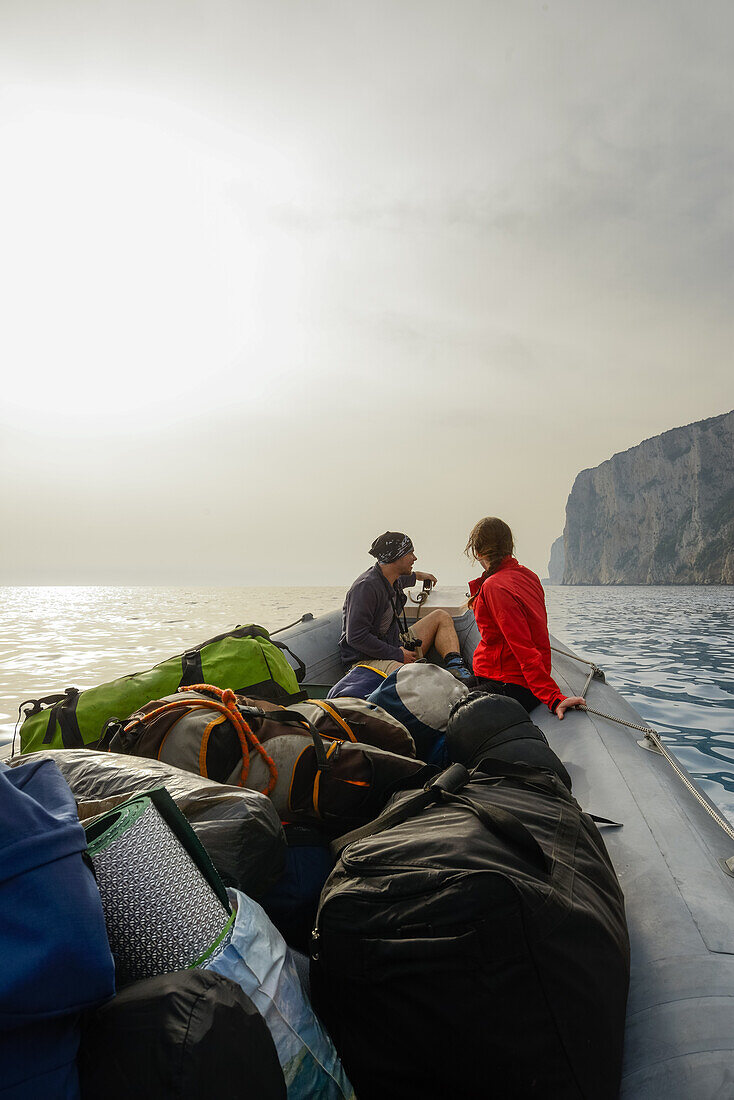 Junge Frau und junger Mann sitzen mit Trekkingausrüstung im Bug eines Schlauchboot das sie zurück zum Ausgangspunkt des Selvaggio Blu bringt, Golfo di Orosei, Sardinien, Italien, Europa