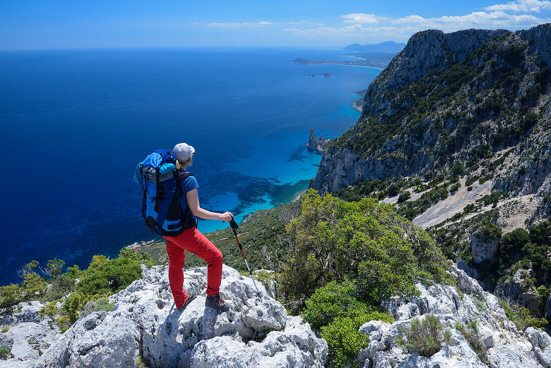 Eine junge Frau wandert entlang der gebirgigen Küste, Felsnadel bei Pedra Longa und Santa Maria Navarrese im Hintergrund, Punta Giradili, Selvaggio Blu, Sardinien, Italien, Europa