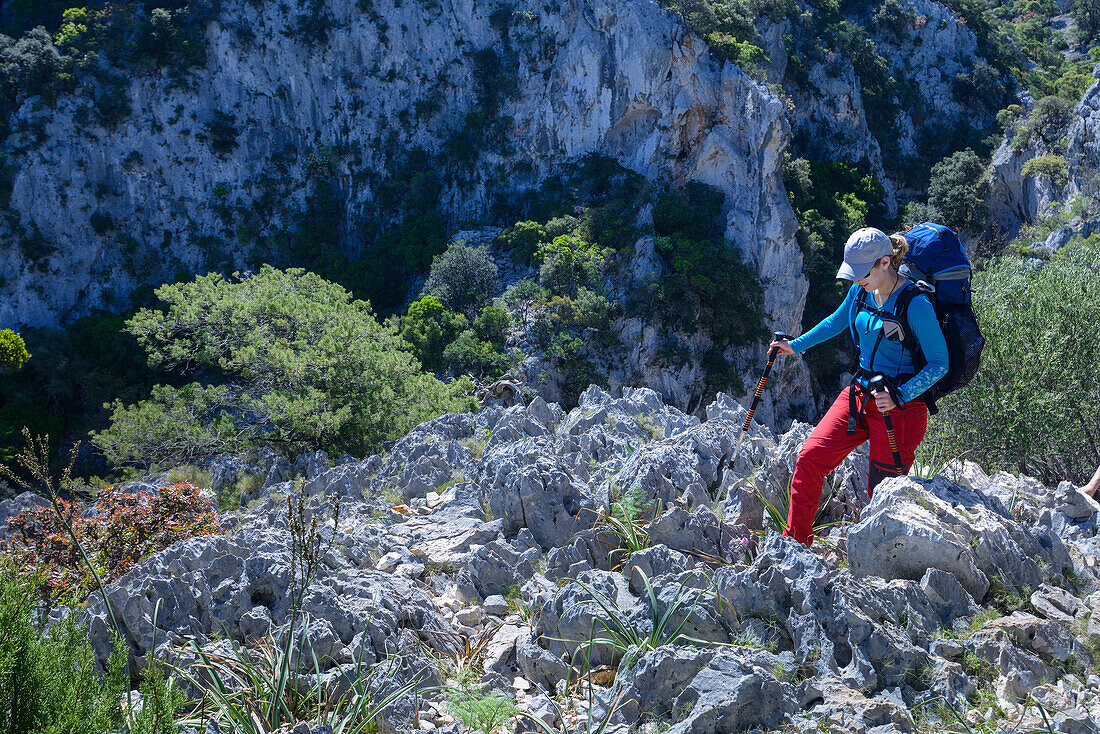 Eine junge Frau mit Trekkingausrüstung wandert durch die gebirgige Küstenlandschaft, Selvaggio Blu, Sardinien, Italien, Europa