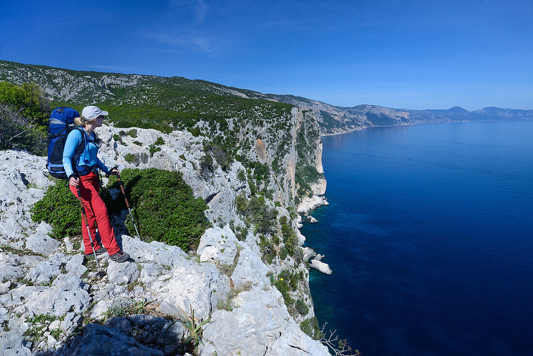 Eine junge Frau mit Trekkingausrüstung wandert oberhalb des Meeres entlang der gebirgigen Küste, Selvaggio Blu, Sardinien, Italien, Europa