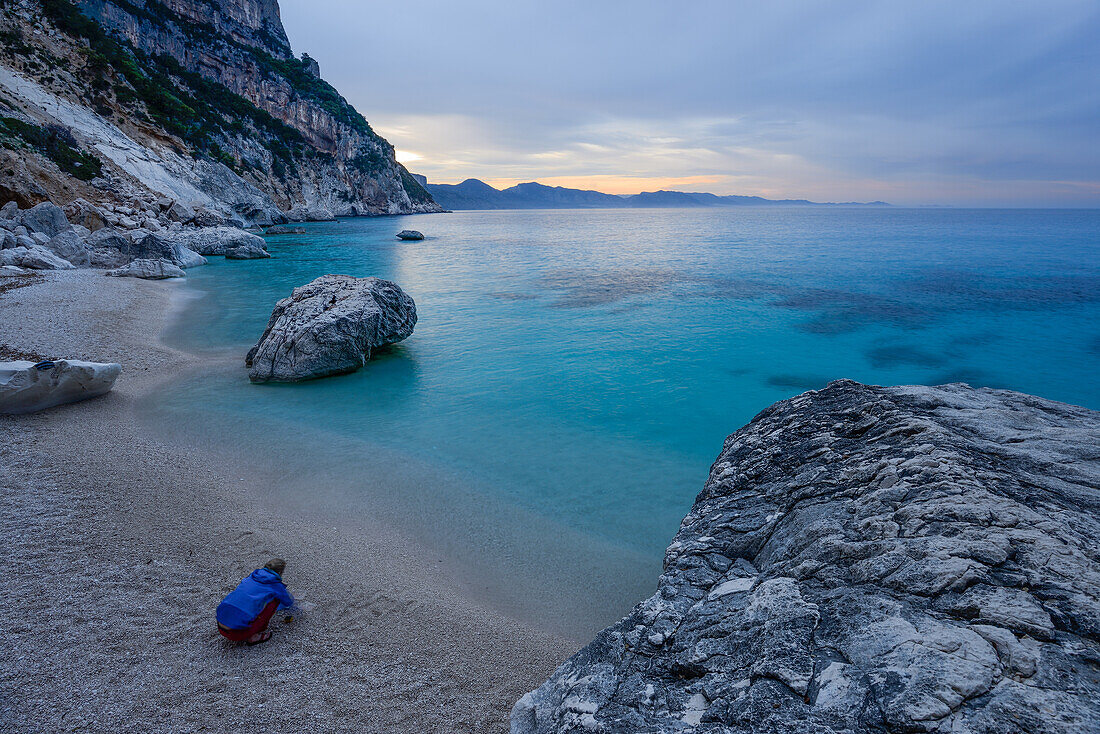 Eine junge Frau kocht Abendessen am Strand der Cala Goloritze am Meer, Golfo di Orosei, Selvaggio Blu, Sardinien, Italien, Europa