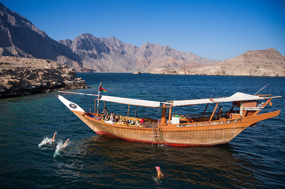 Menschen springen von Dhau Boot ins Wasser nahe Telegraph Island in einem Fjord der Musandam Halbinsel, nahe Khasab, Oman
