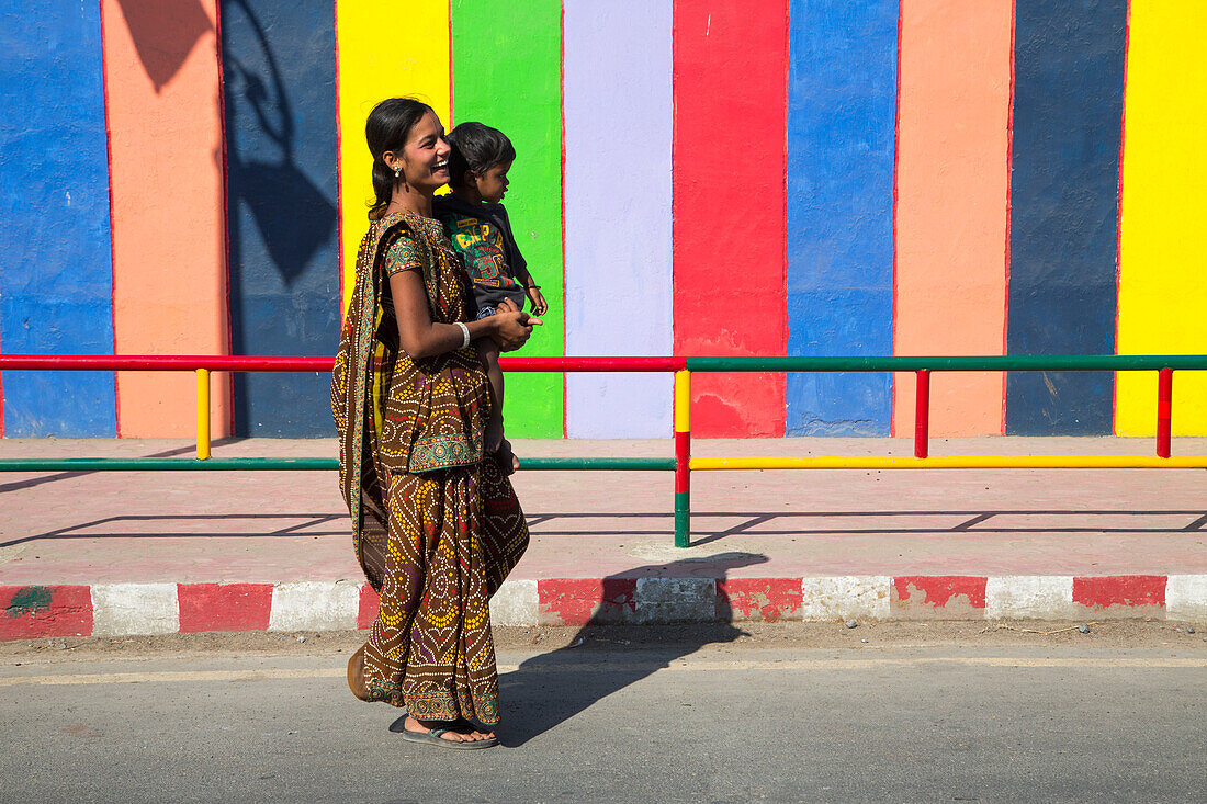 Junge Frau mit Kind vor farbenfroher Wand mit Schatten von Lampen, Insel Diu, Daman and Diu, Indien