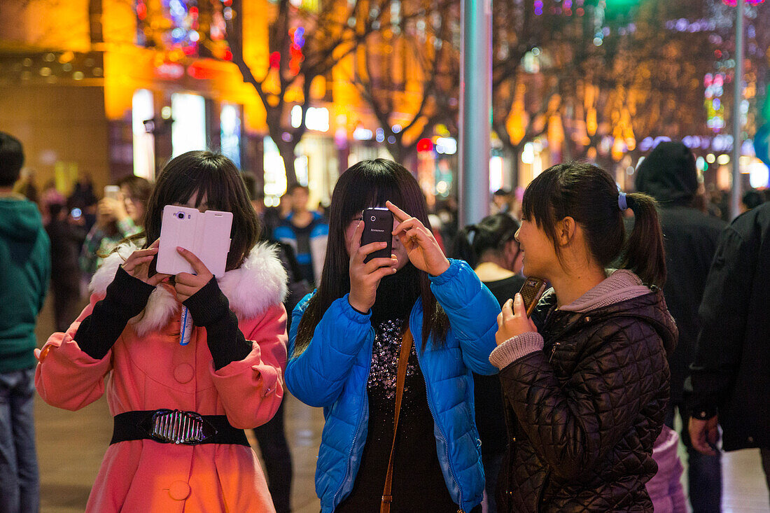 Teenage girls take photographs with smartphones at Nanjing Road pedestrian zone, Shanghai, China