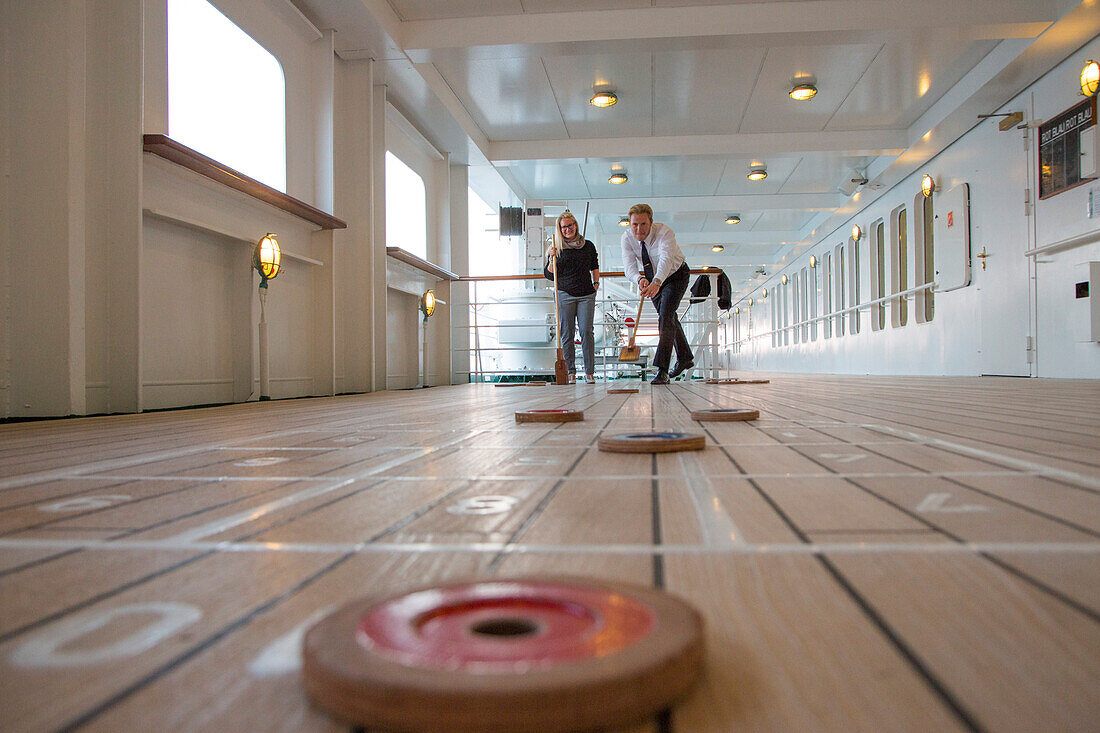 Junges Paar spielt Shuffleboard an Bord von Kreuzfahrtschiff MS Deutschland (Reederei Peter Deilmann), Nordsee, nahe Deutschland, Europa