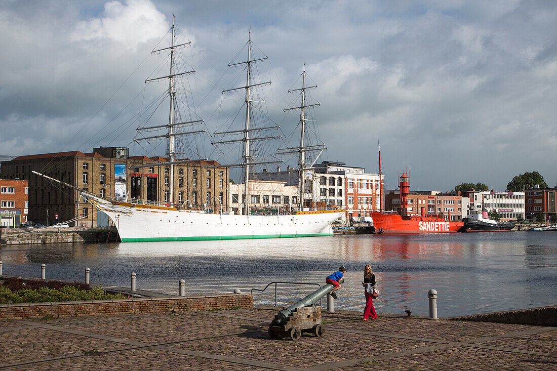 Child climbs on cannon at Bassin du Commerce with view of sailing ship Duchesse Anne and historic lightship Sandettie, Dunkirk, Nord-Pas-de-Calais, France