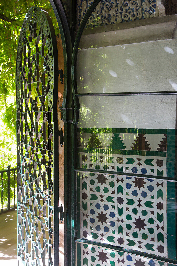 Geöffnete Tür zum Garten und Kacheln mit geometrischem Muster der Mauren an einer Wand im Alcazar Königspalast, Sevilla, Andalusien, Spanien, Europa