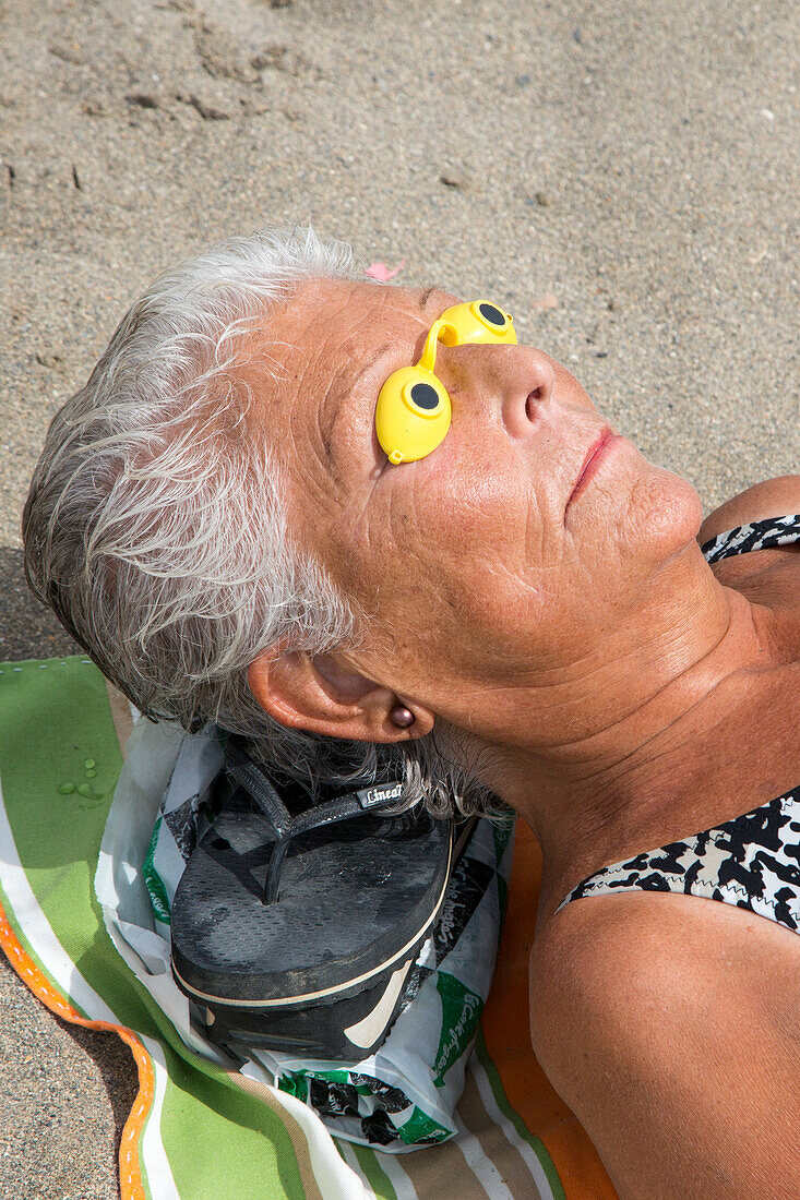 Ältere Frau schützt ihre Augen bei Sonnenbad am Strand Playa de la Malagueta, Malaga, Andalusien, Spanien, Europa