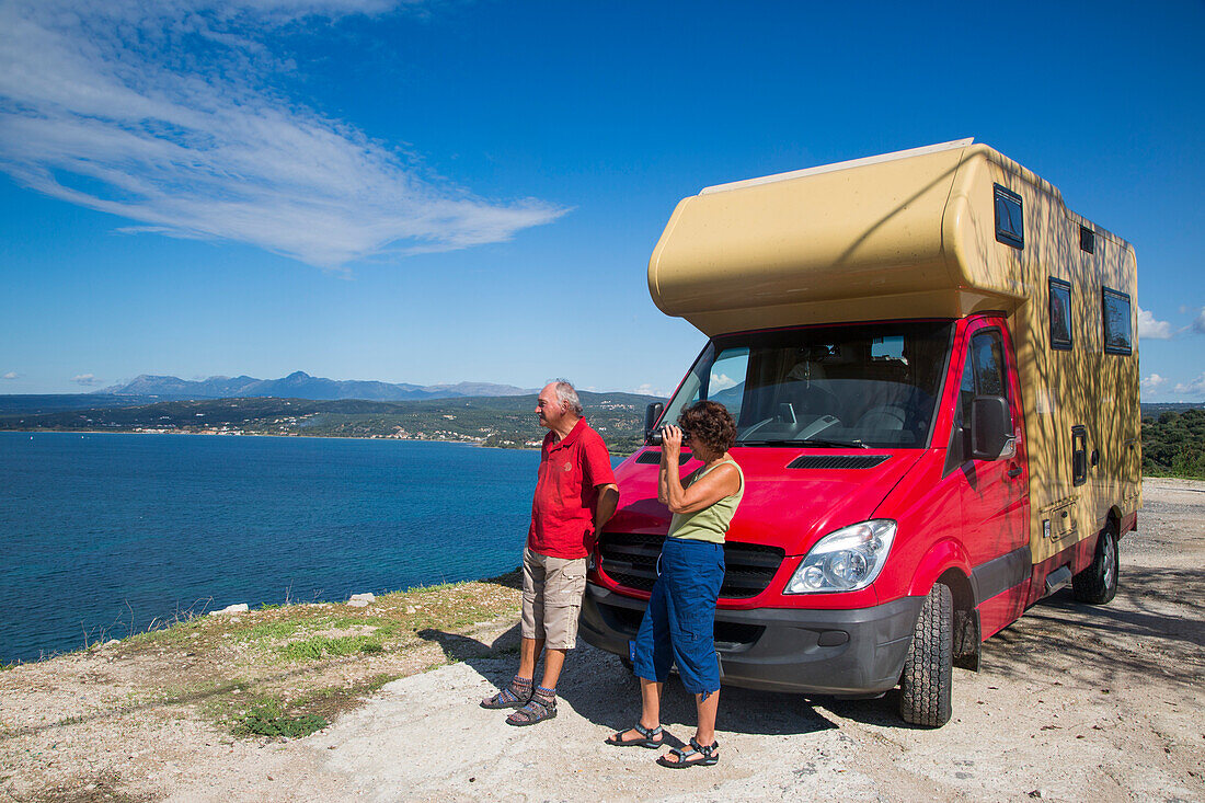 Paar steht vor rotem Wohnmobil und blickt auf das Meer, Pylos, Peloponnese, Griechenland, Europa