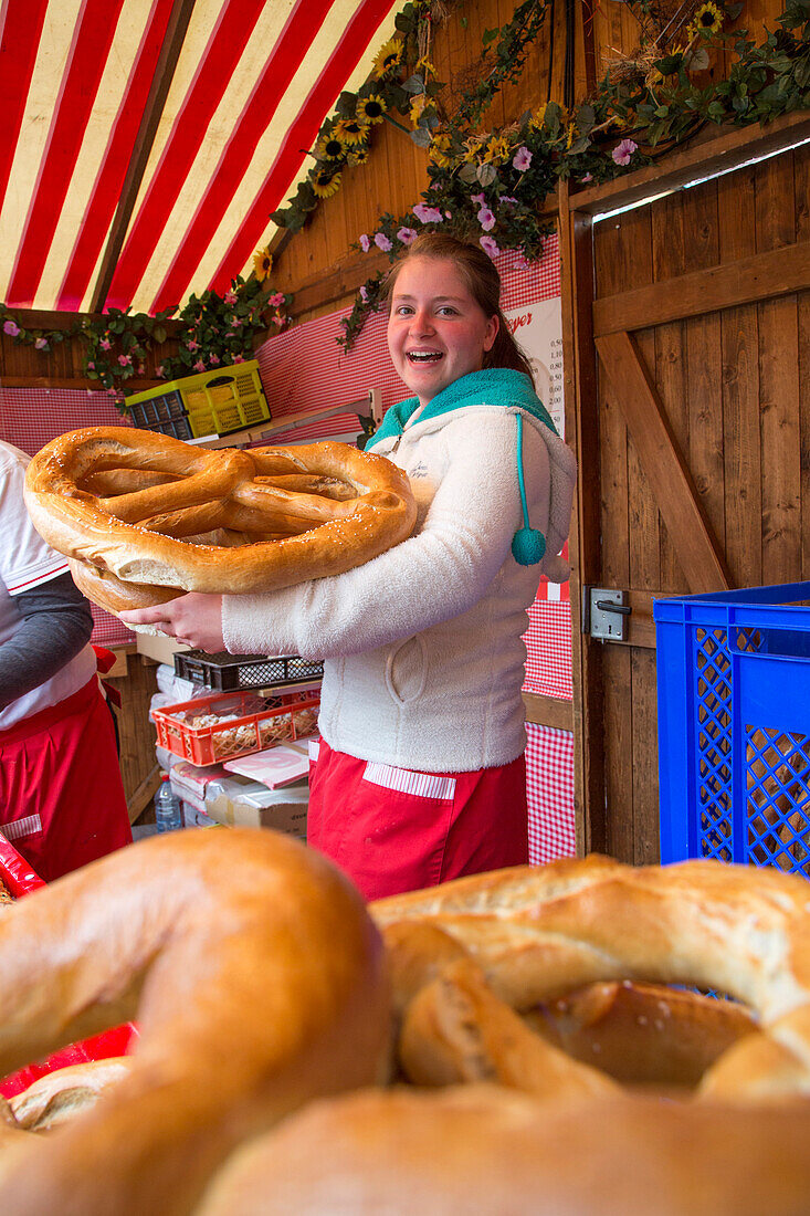 Young woman presents giant pretzels for sale at Bergbrezen food stall at Erlanger Bergkirchweih beer festival and fair, Erlangen, Franconia, Bavaria, Germany