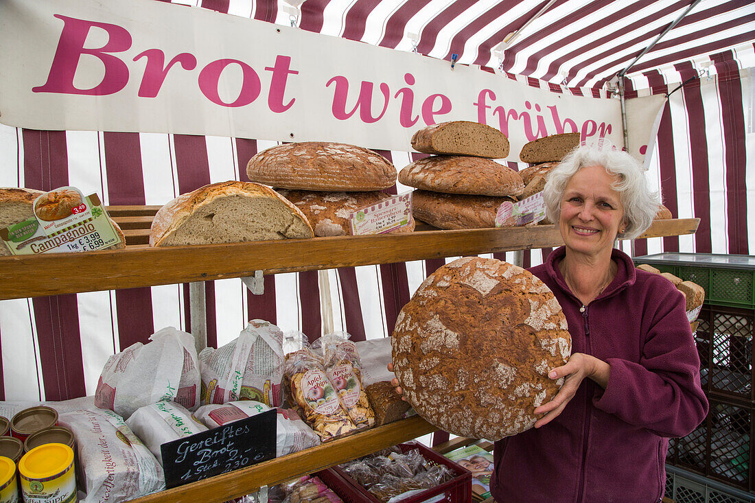 Woman presents large loaf of bread at Lebe Gesund market stand at the Farmer's Market on Marktplatz market square, Erlangen, Franconia, Bavaria, Germany