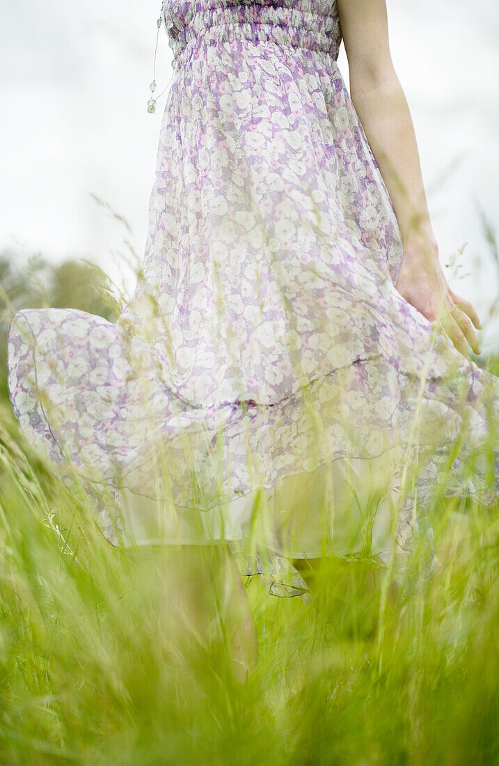 Woman standing in grassy field, dress blowing in wind, cropped view
