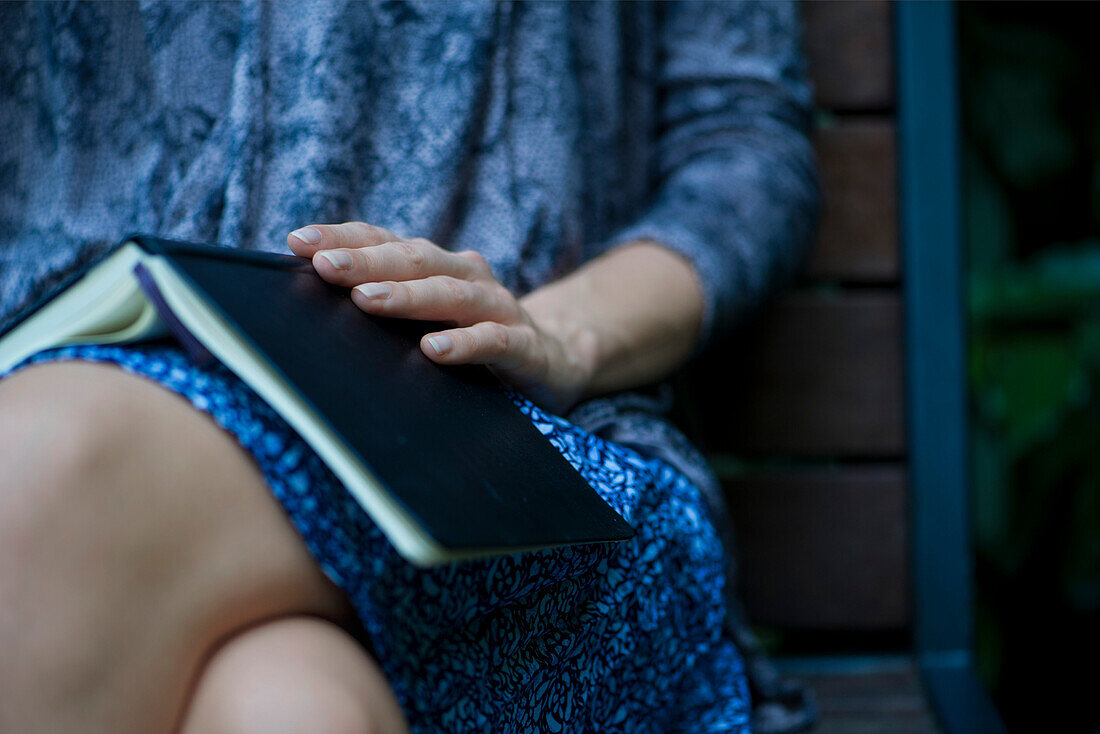Woman sitting with open book resting on lap, cropped