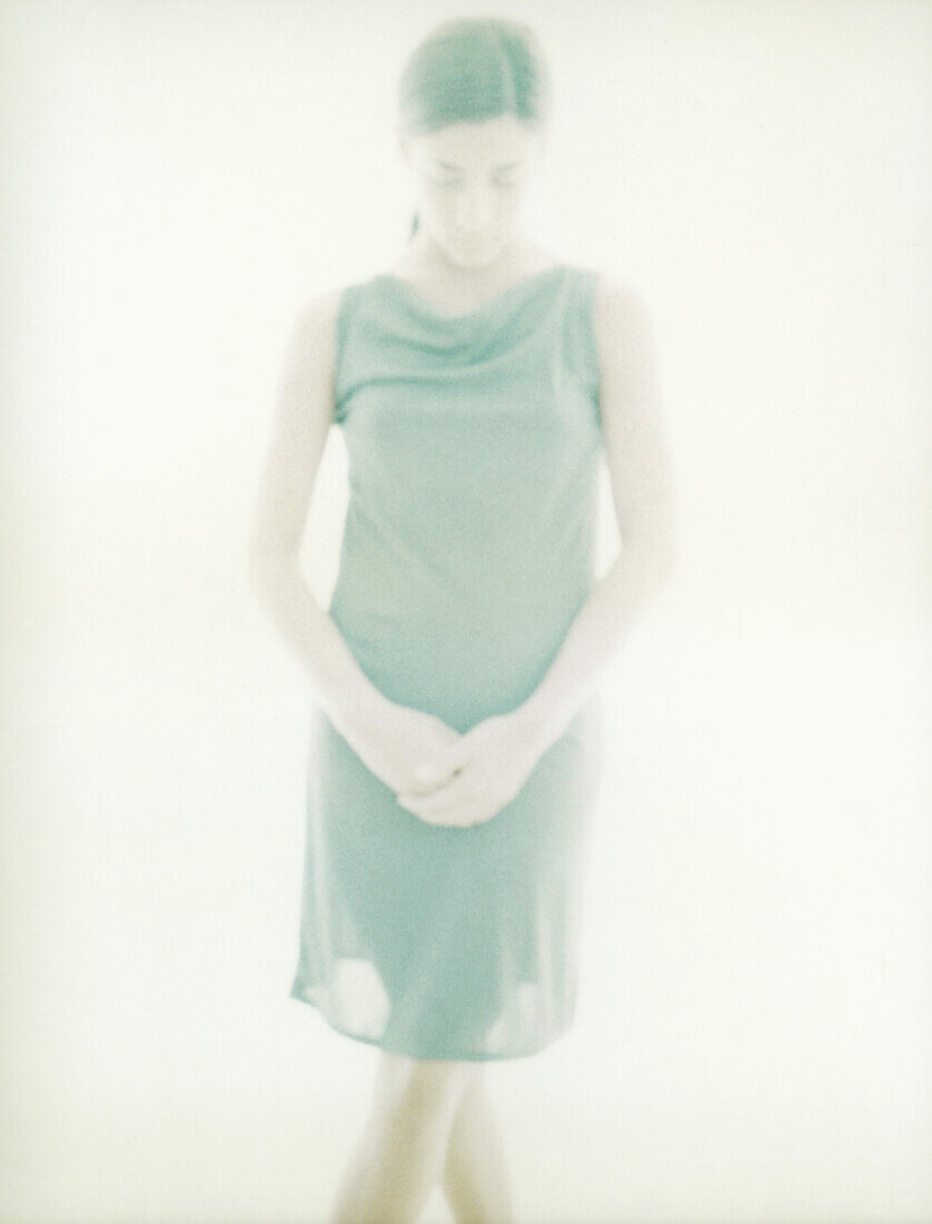 Young woman standing with hands clasped, overexposed