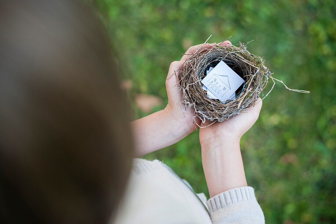 Child's hands holding bird nest containing drawing of house
