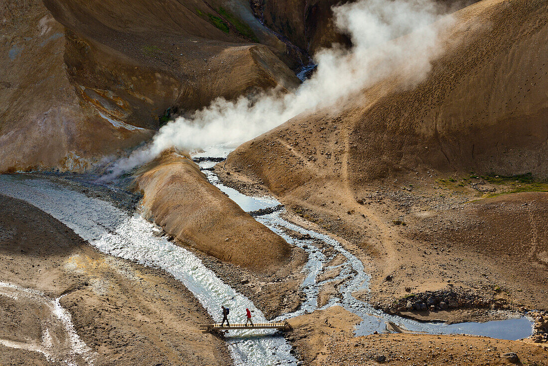 Wanderer gehen über Brücke im Geothermalgebiet Hveradalir, Dampf steigt farbigen Rhyolith-Bergen, Vulkangebirge Kerlingarfjöll, Hochland, Südisland, Island
