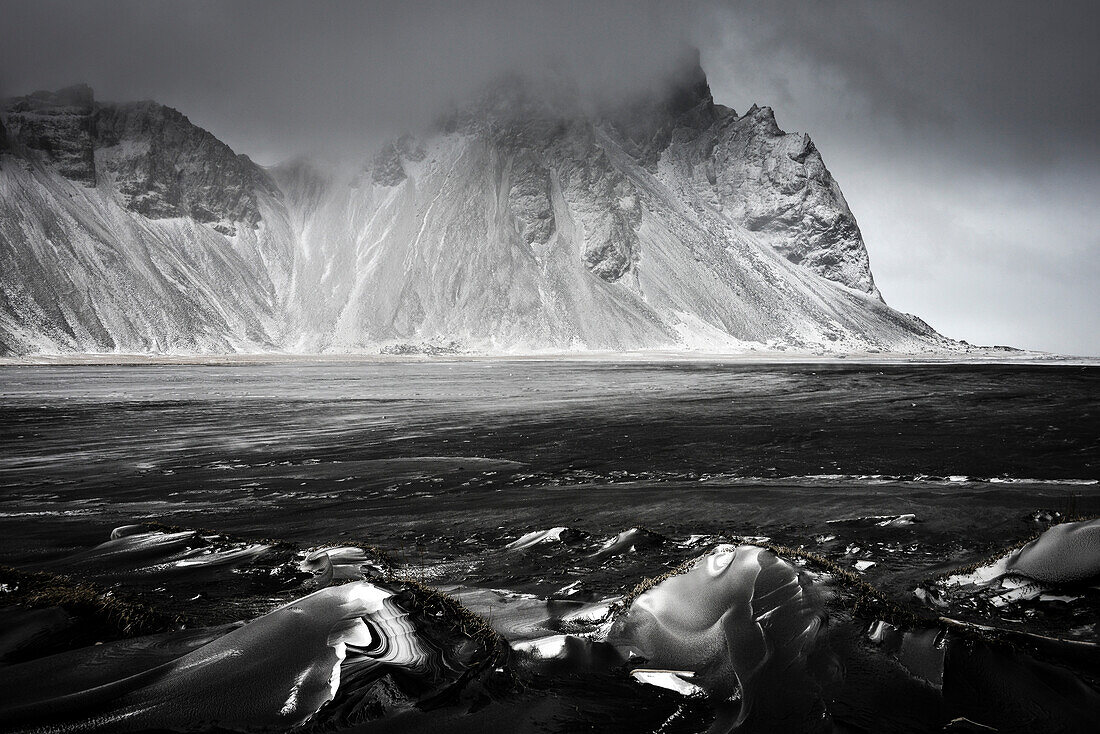 Black obsidian (volcanic glass) at winterly peninsula Stokksnes with mountain range Klifatindur and peak Vesturhorn (Vestrahorn), coastal flat plains near Hofn, East Iceland, Iceland, Europe