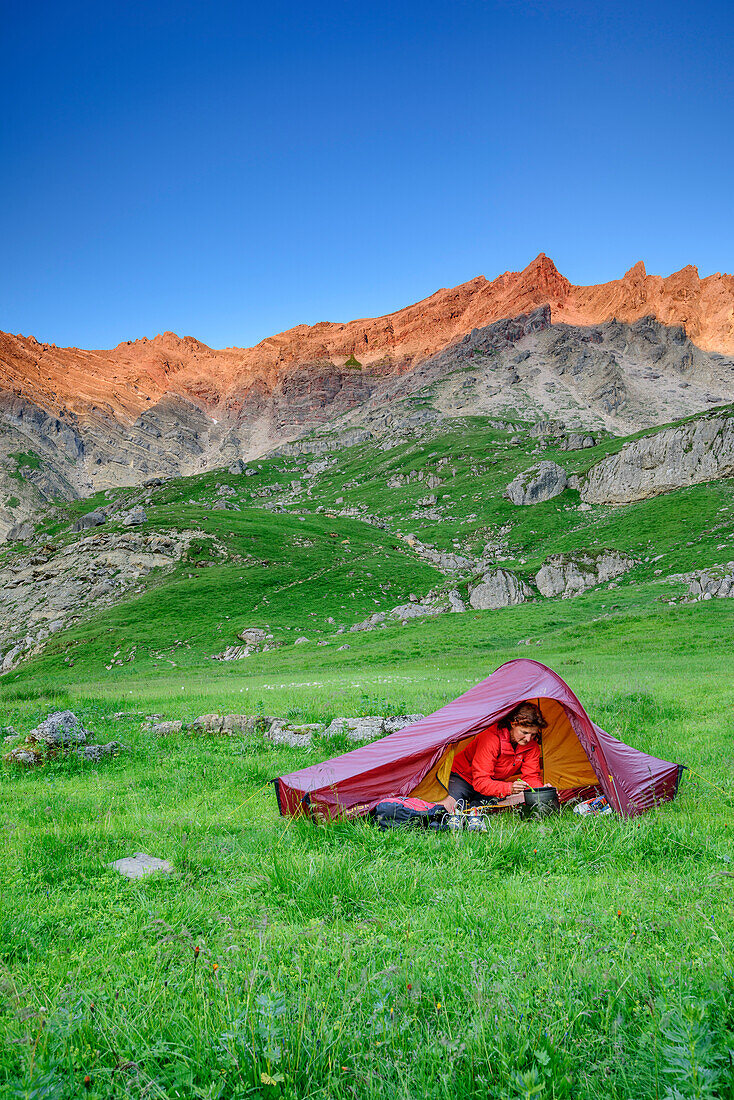 Woman sitting in tent and eating, Lechtal Alps in alpenglow in background, valley Fundaistal, Lechtal Alps, Tyrol, Austria