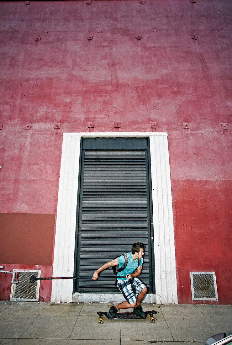 Caucasian man riding skateboard with land paddle, Los Angeles, California, USA