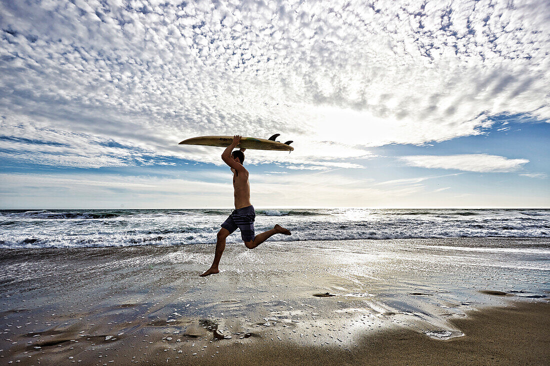 Caucasian man jumping with surfboard on beach, Los Angeles, California, USA