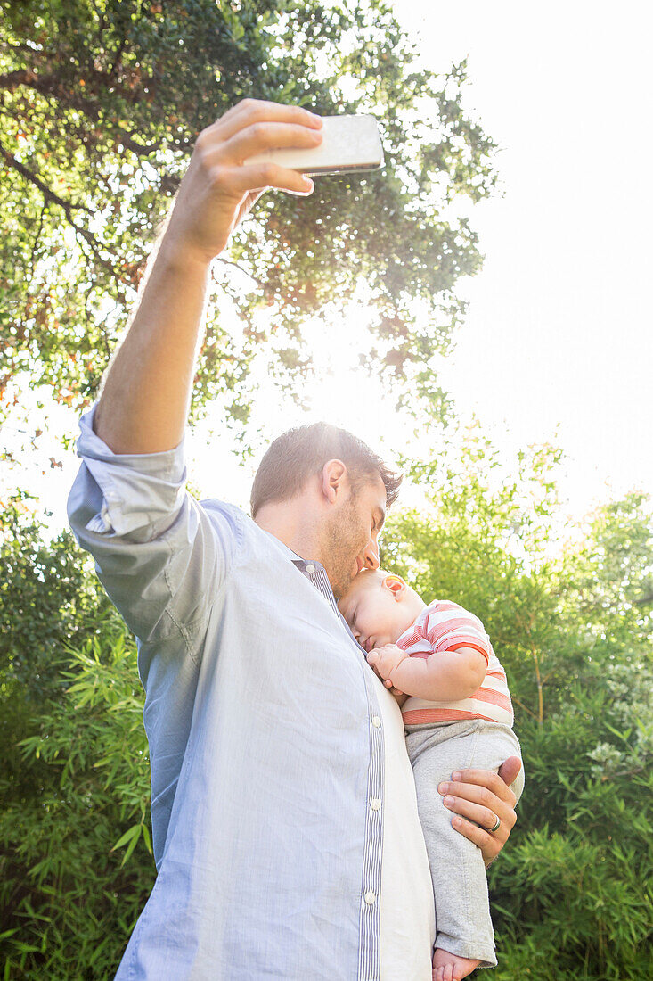 Caucasian father taking cell phone picture with baby in backyard, Los Angeles, California, USA