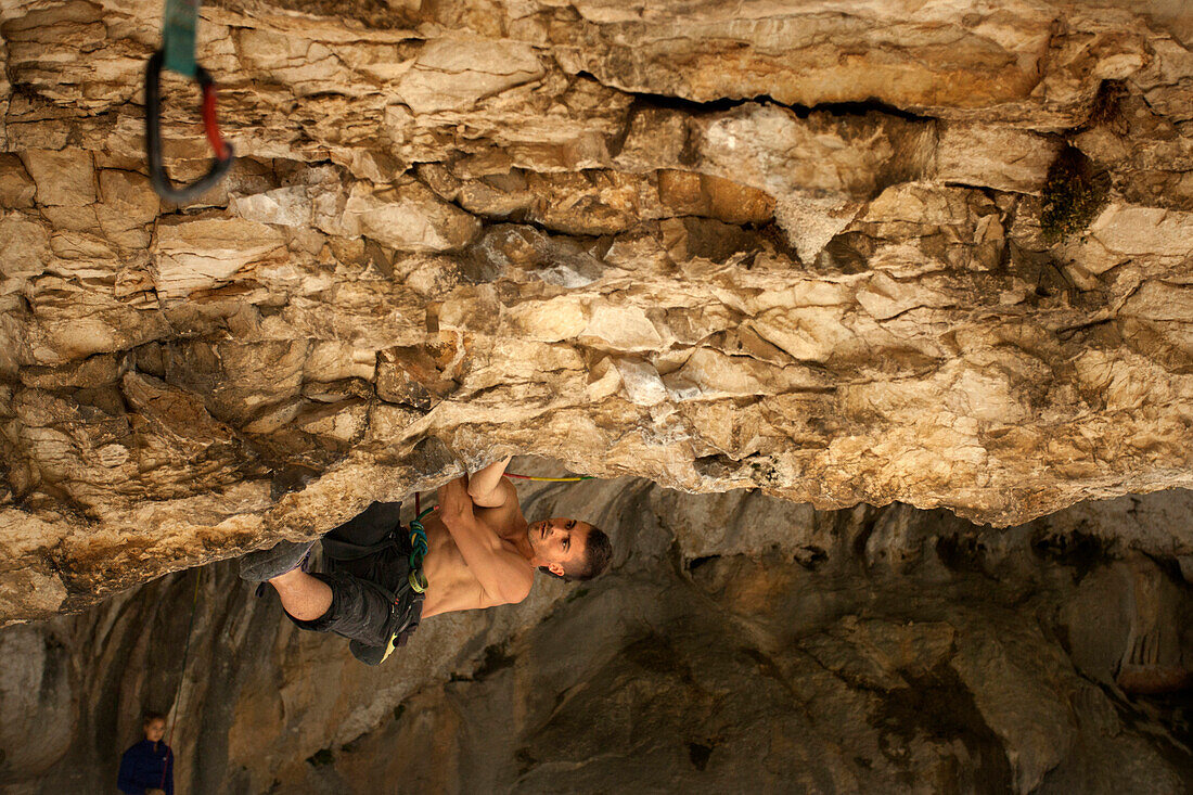 Climber hanging from rocky cave ceiling, Rodellar, Aragon, Spain