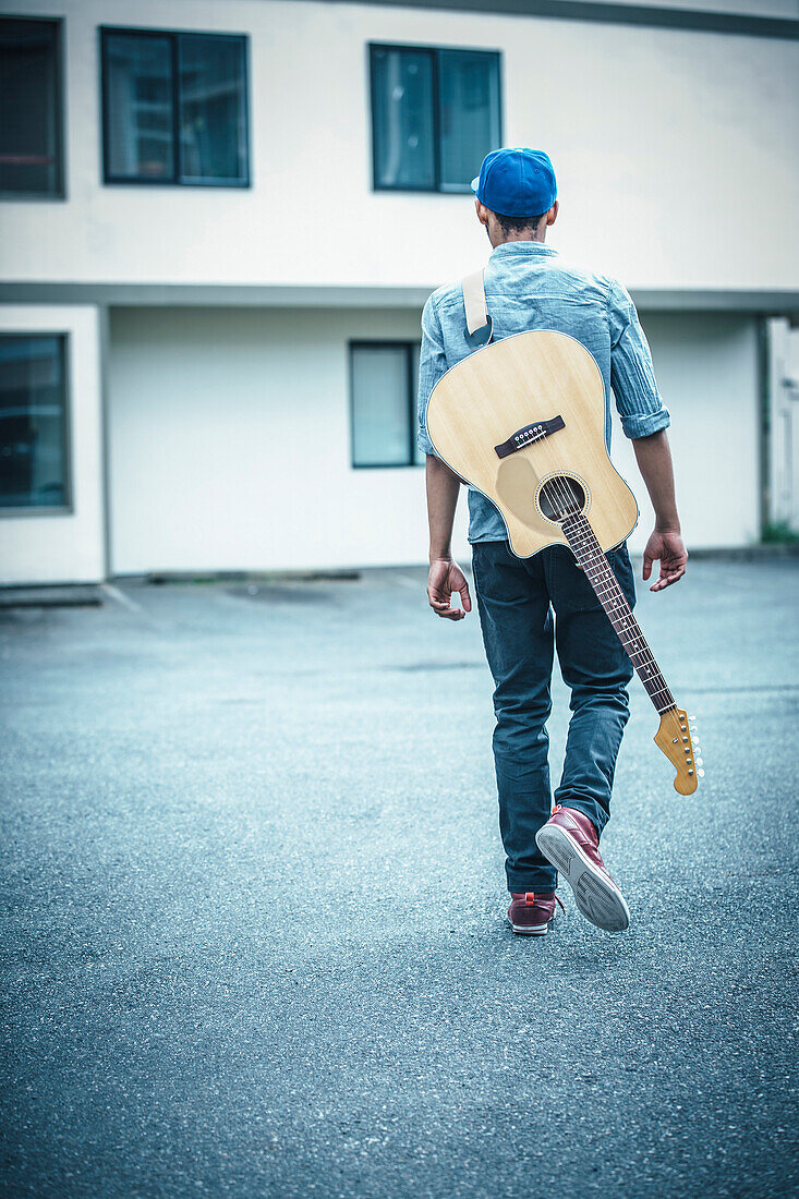 Mixed race boy carrying guitar in parking lot, Seattle, WA, USA