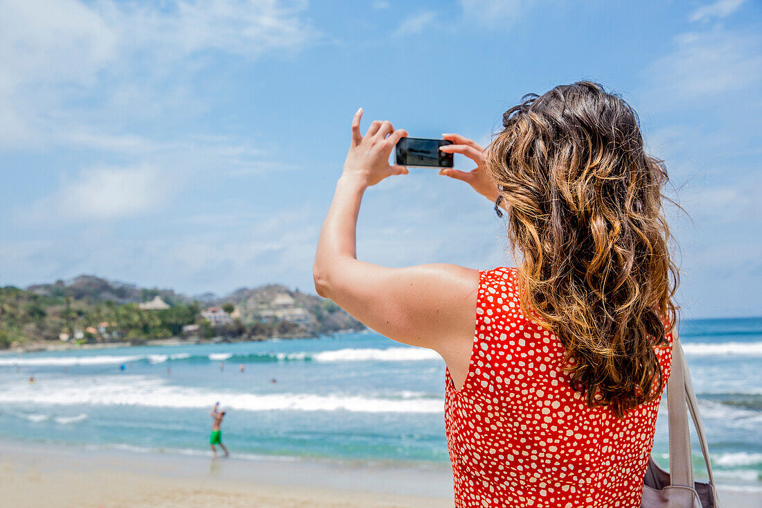 Mixed race woman taking pictures of tropical beach, Sayulita, Jalisco, Mexico
