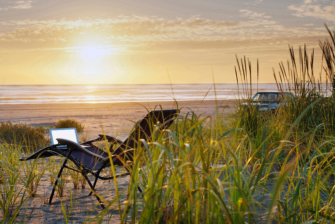 Laptop on deck chair overlooking sunset on beach, C1