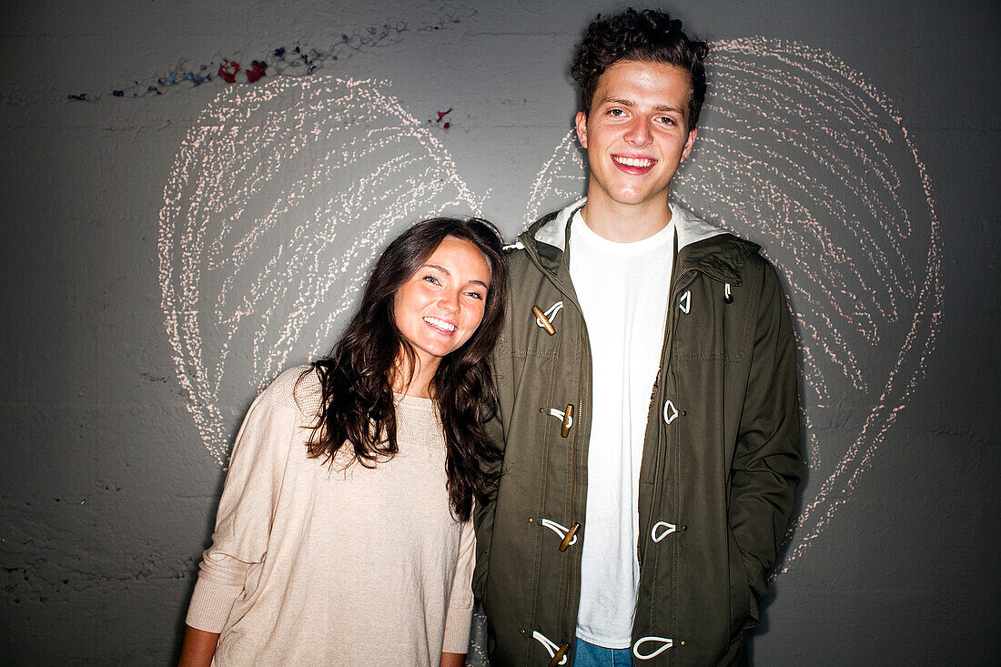 Caucasian couple smiling near chalk heart on wall, Seattle, Washington, United States