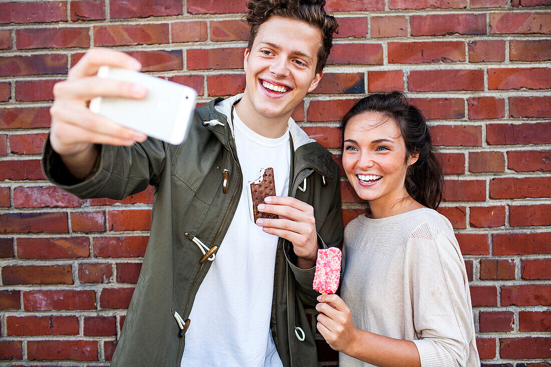 Caucasian couple taking selfie near red brick wall, Seattle, Washington, United States