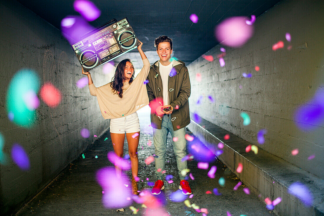 Caucasian couple carrying boom box and throwing confetti in tunnel, Seattle, Washington, United States