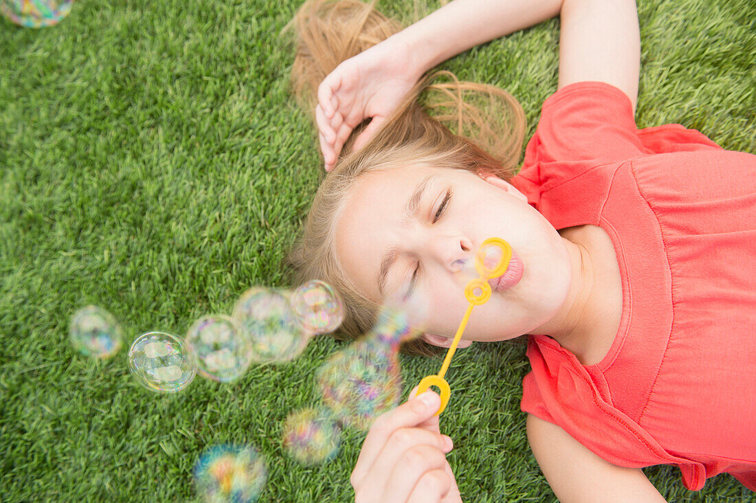 Caucasian girl blowing bubbles on grassy lawn, Jersey City, New Jersey, USA