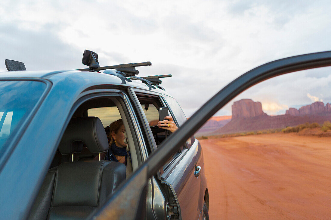 Caucasian girl taking cell phone photograph from car, Monument Valley, Utah, United States, Monument Valley, Utah, USA
