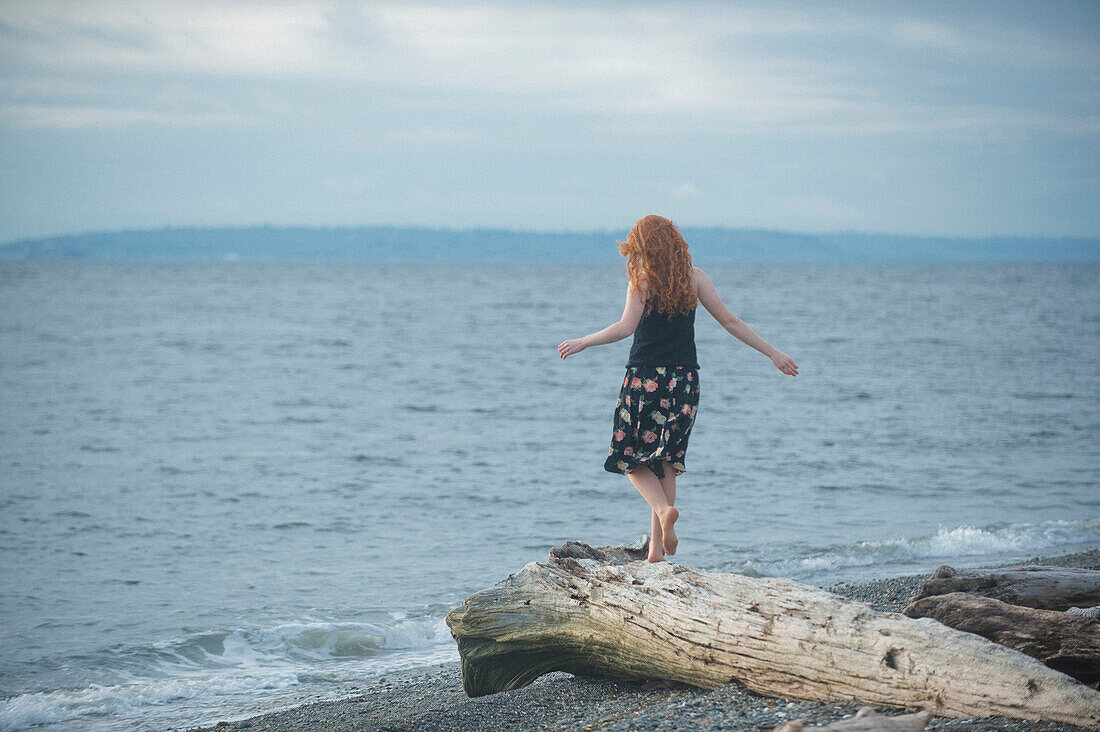 Girl walking on driftwood on beach, Bainbridge Island, WA, USA
