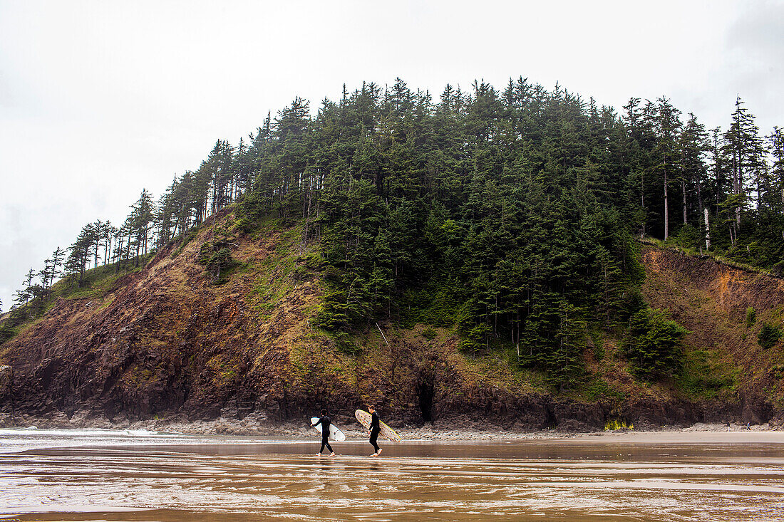 Surfers carrying surfboards on beach, Cannon Beach, Oregon, United States