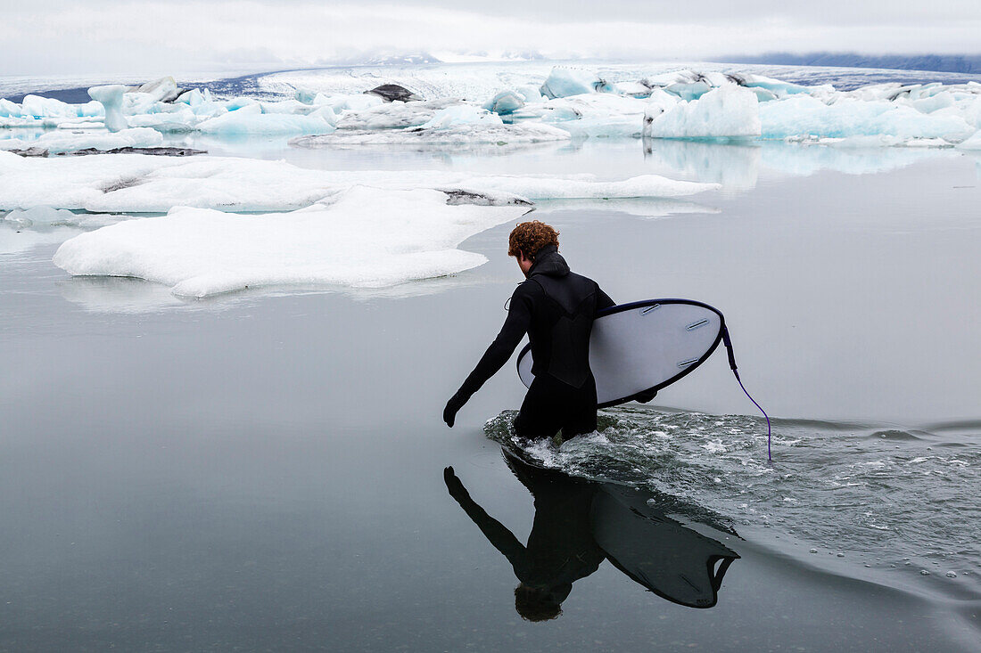 Caucasian surfer carrying board in glacial water, Jokulsarlon, Iceland, Iceland