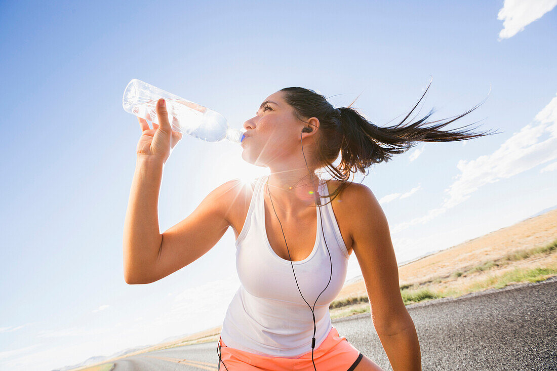 Caucasian runner drinking water bottle on remote road, Little Sahara, Utah, USA