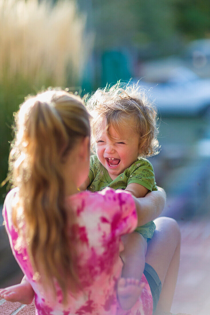 Caucasian sister holding laughing baby brother outdoors, Santa Fe, New Mexico, USA